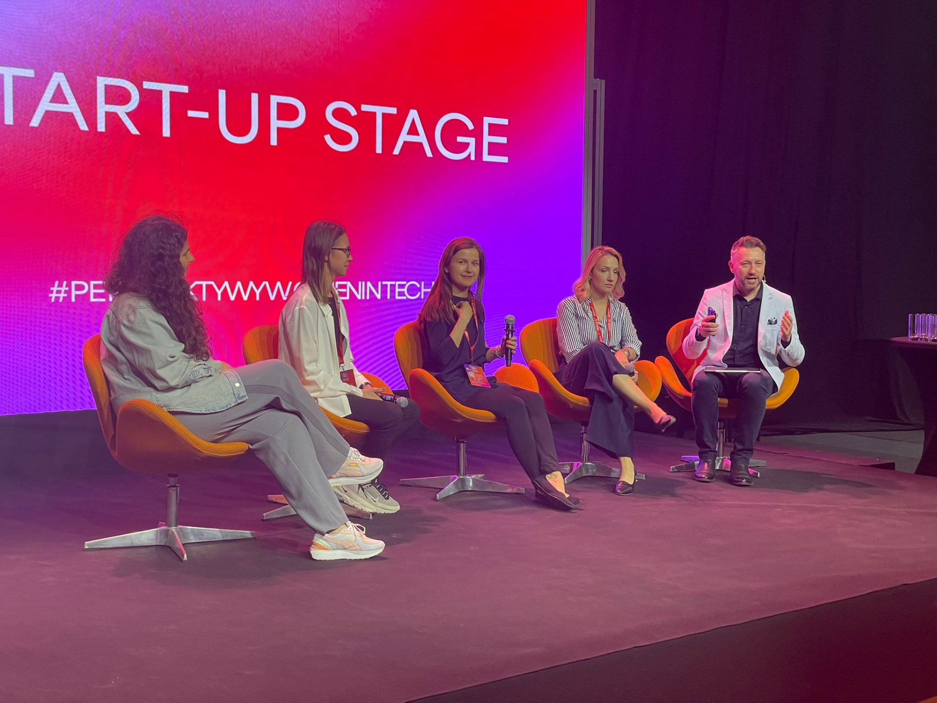 Andrew Wrobel, in a white blazer, speaking on a five-person panel on the Start-Up Stage at the Perspektywy Women in Tech Summit in Warsaw