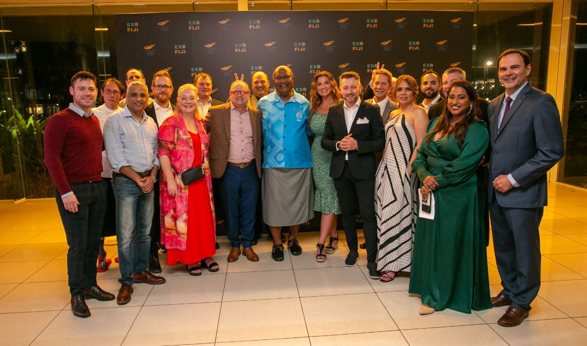 Andrew Wrobel, in traditional Fijian formal dress, at the centre of a group of delegates in front of the Exo Fiji and Outsource Fiji backdrop