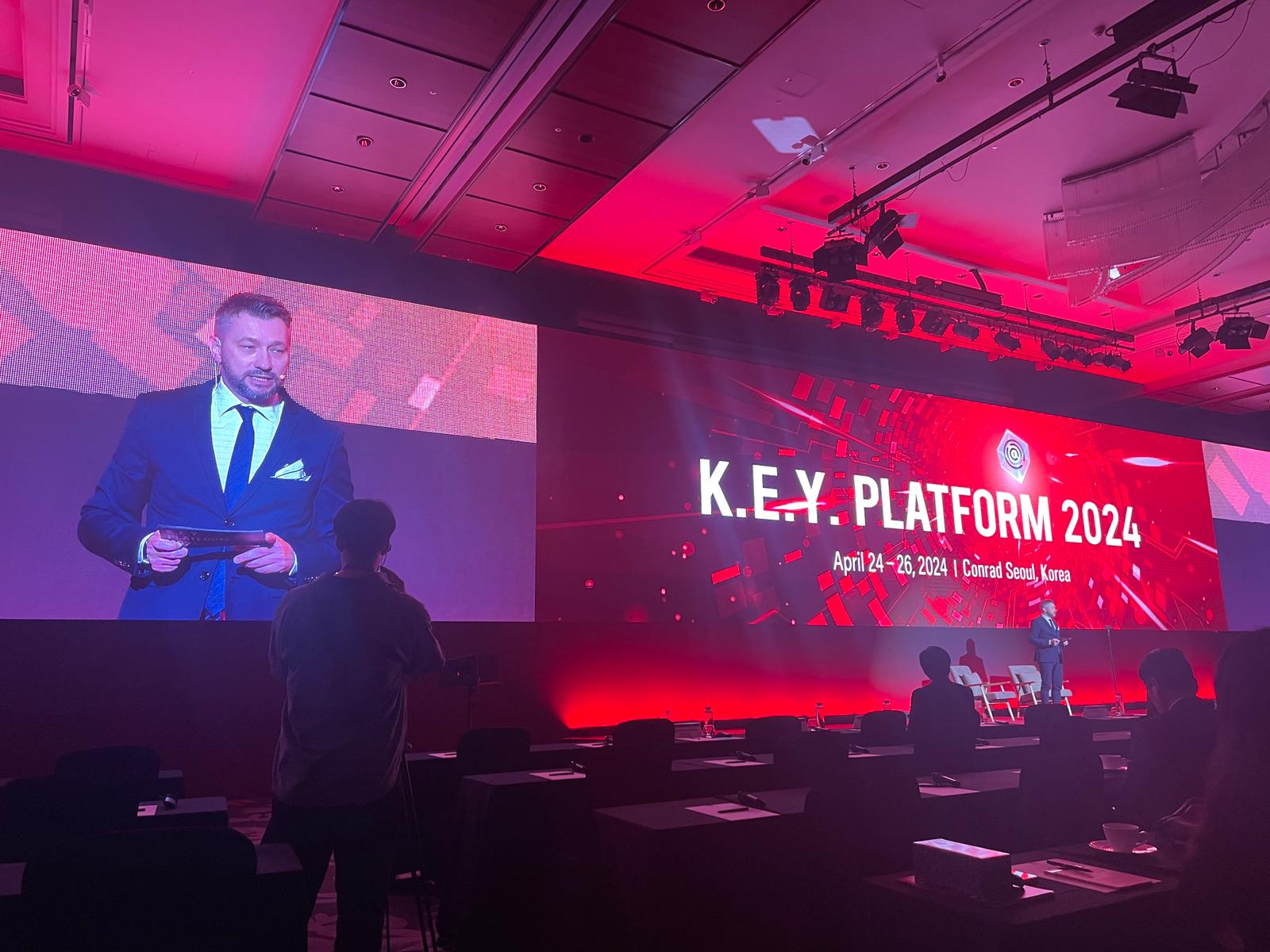 Andrew Wrobel on stage at K.E.Y. Platform 2024 at the Conrad Seoul in Korea, with the event screen and a close-up of him projected behind the stage