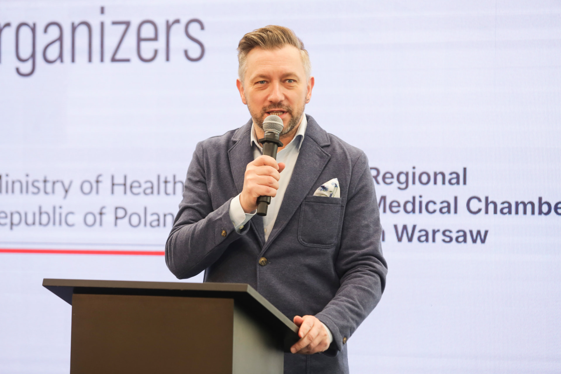 Andrew Wrobel speaking at the European Health Data & Innovation Summit in Warsaw, with the Ministry of Health and Regional Medical Chamber in Warsaw behind him
