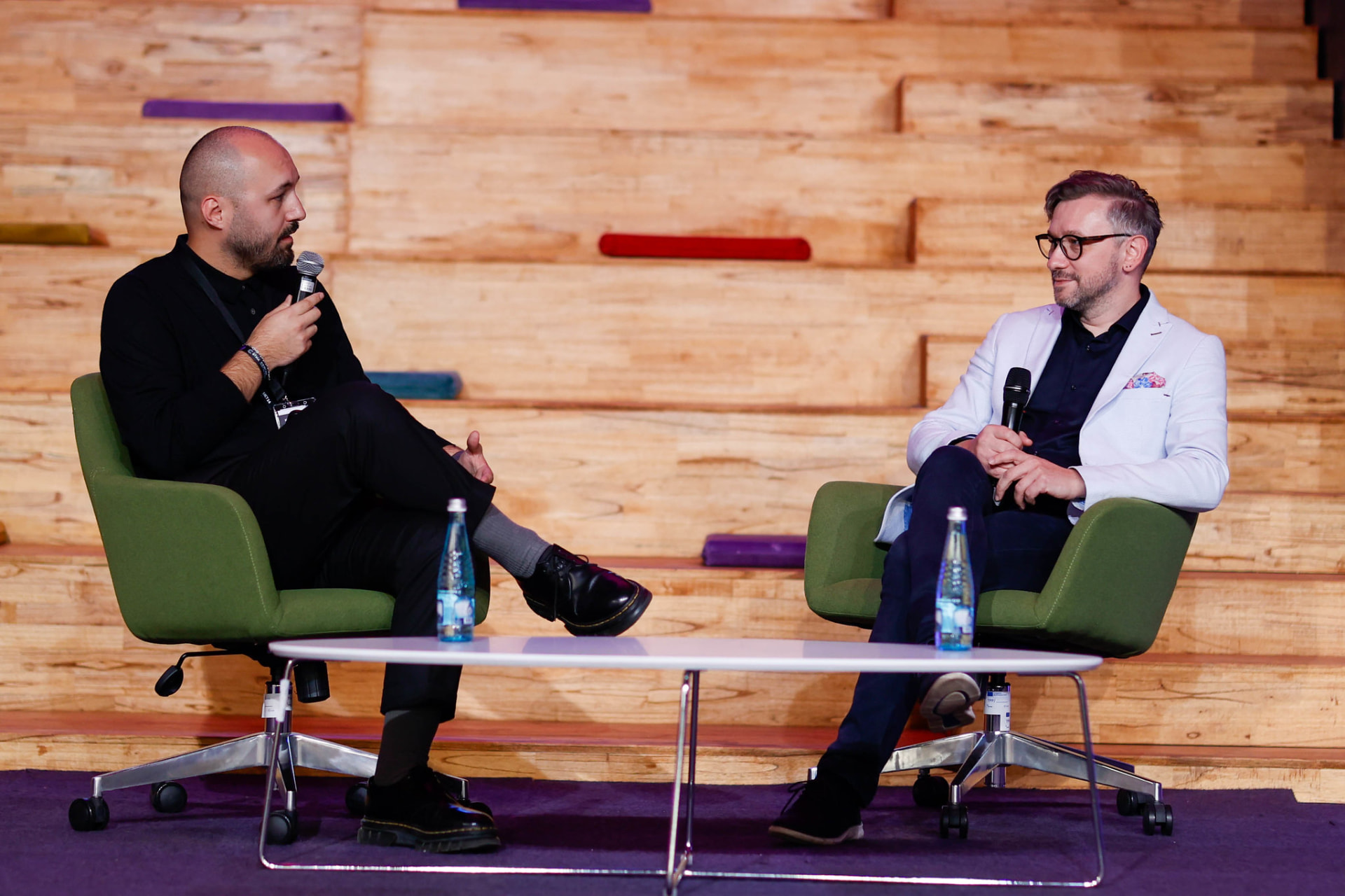 Andrew Wrobel in conversation in an armchair on stage at the KosICT Festival in Prishtina, with the Emerging Europe screen behind him